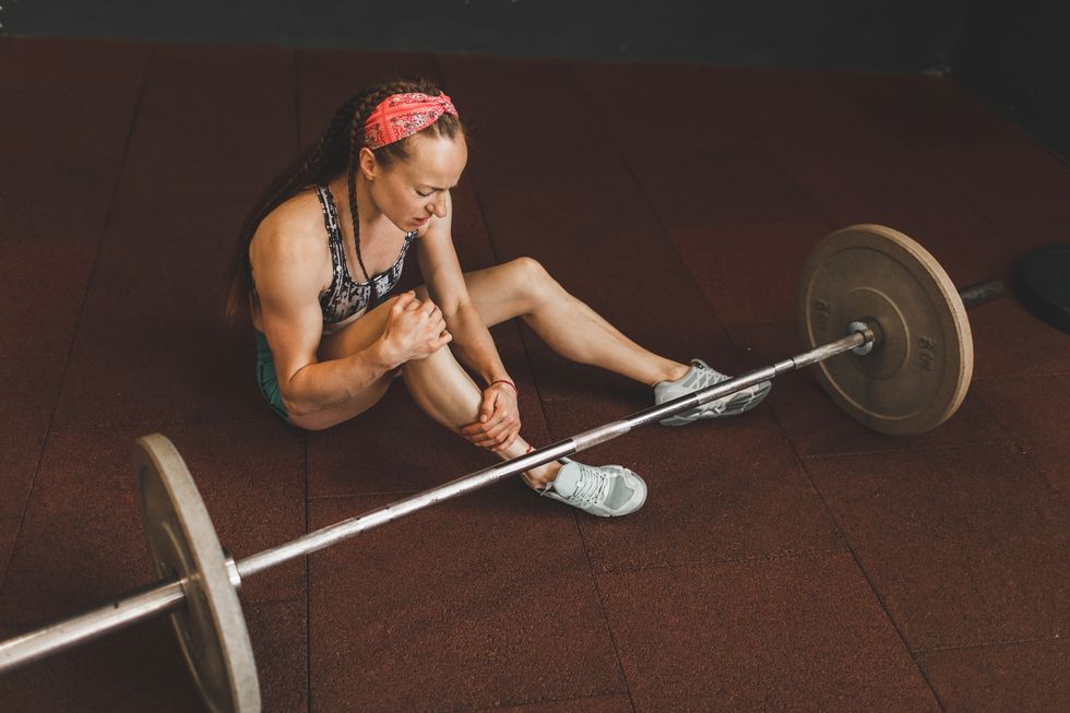 knee injury of woman lifting barbell in gym health problem, sprain ligament, stress and pain