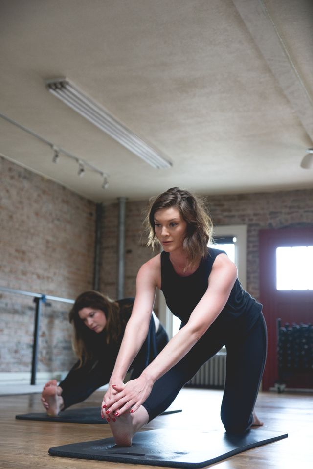 women doing a hamstring stretch in a barre of yoga workout