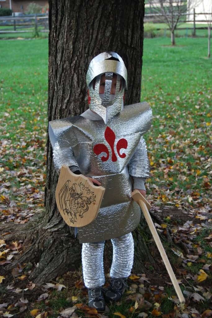 diy full body knight in shining armor costume worn by tween boy, about 9 or 10 years old, leaning against a tree