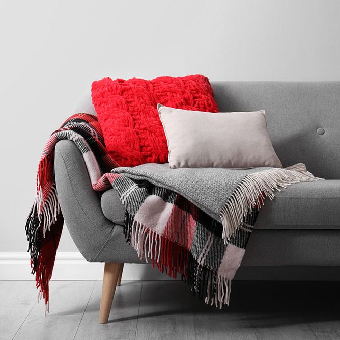 sofa with soft pillows and warm plaids near light wall indoors