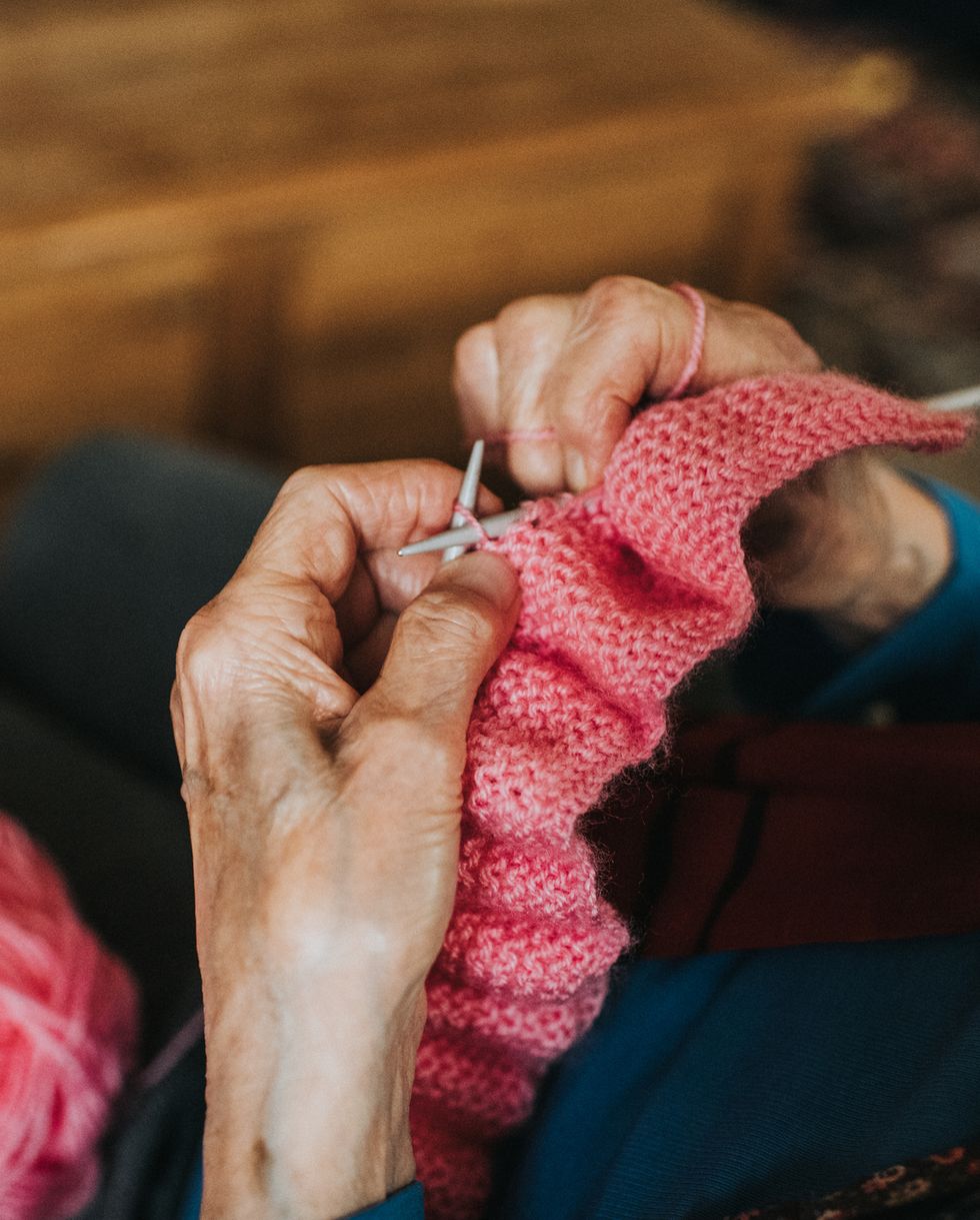 elderly woman knitting a pink blanket