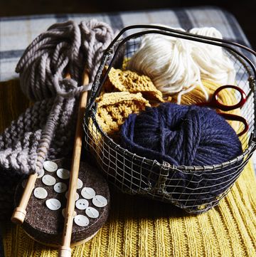 balls of blue and white wool in small wire basket, wooden knitting needles, buttons, placed on yellow ribbed knitted fabric, texture