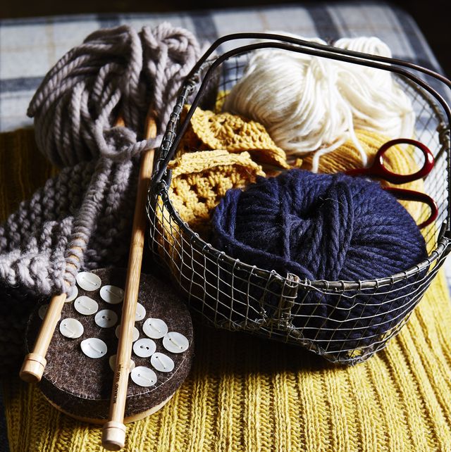 balls of blue and white wool in small wire basket, wooden knitting needles, buttons, placed on yellow ribbed knitted fabric, texture