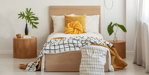 knot pillow and black and white blanket on single bed in fashionable interior with green leaf in vase on wooden nightstand