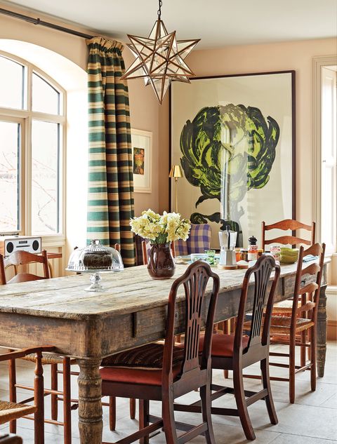 long rustic table surrounded by chairs and backed by a large painting of an artichoke