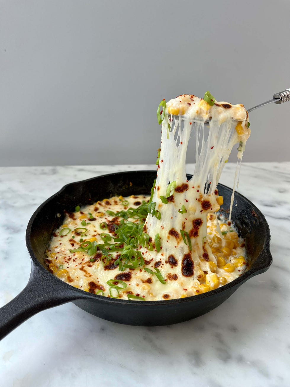 hot cheesy dish with corn and green onions in a cast iron skillet