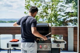 a korean man cooks wings on a gas grill