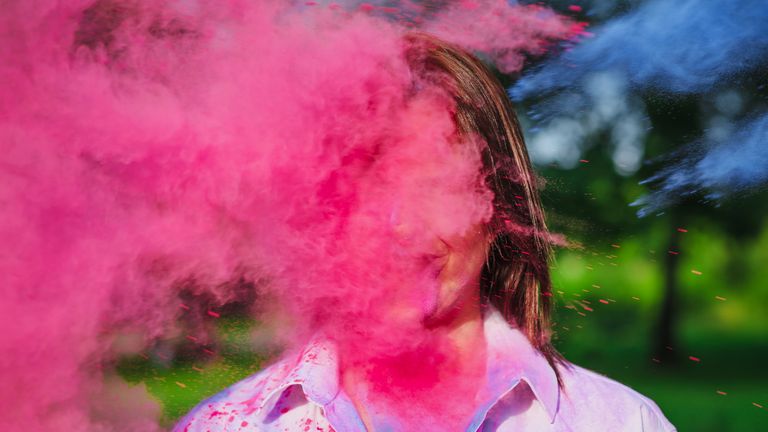 portrait of merry caucasian woman posing in a cloud of a pink  and blue dry paint at holi festival