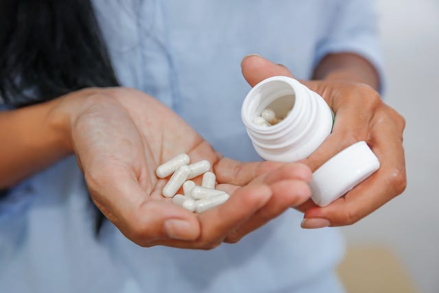 woman holding a pill bottle and white pills in her hands