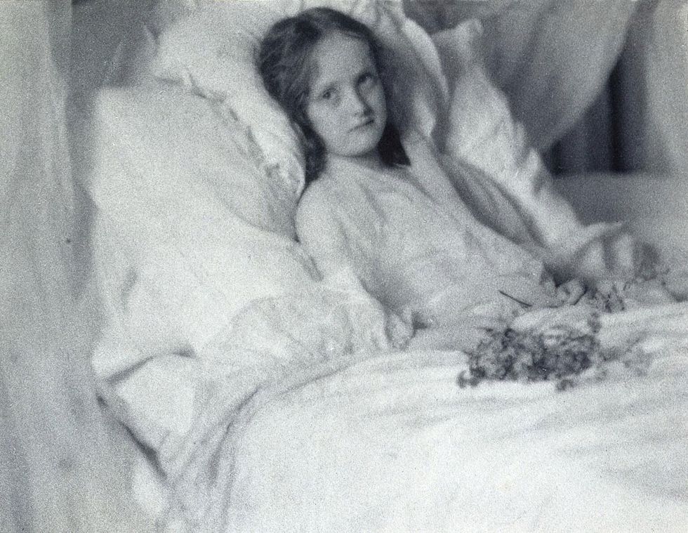 Een meisje dat van een ziekte herstelt ligt in 1904 in bed met bloemen
