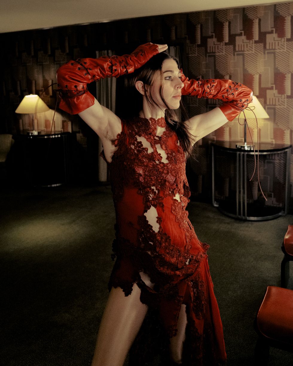 caroline polachek in a dimly lit room wearing a red cut out dress and red fingerless gloves