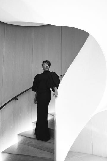individual in a stylish black gown ascending a modern staircase