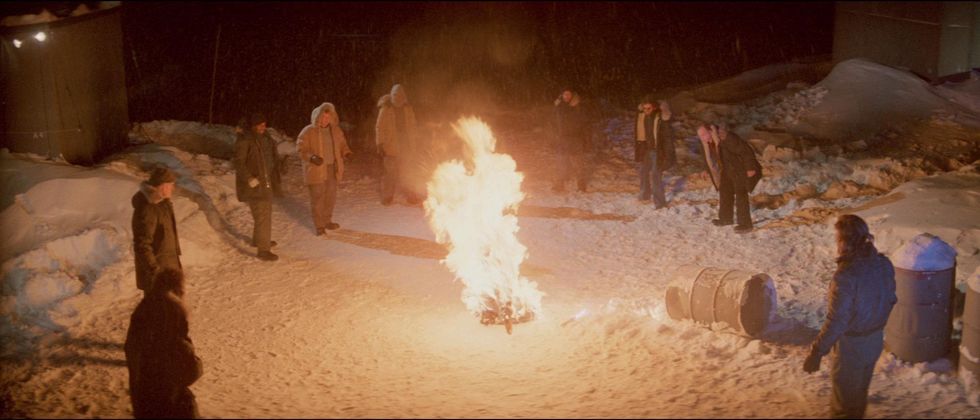 una escena de la cosa de john carpenter en que el equipo quema a la criatura en la nieve haciendo un círculo