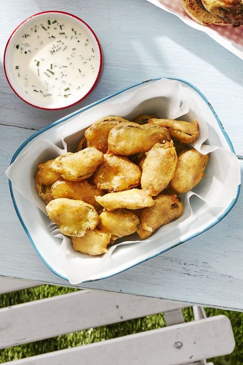 fried pickles in a parchment paper lined serving dish on a white wooden table outside with a small bowl of ranch for dipping