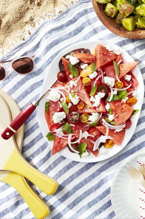 watermelon tomato feta salad on a white oval serving plate on a blanket on the beach