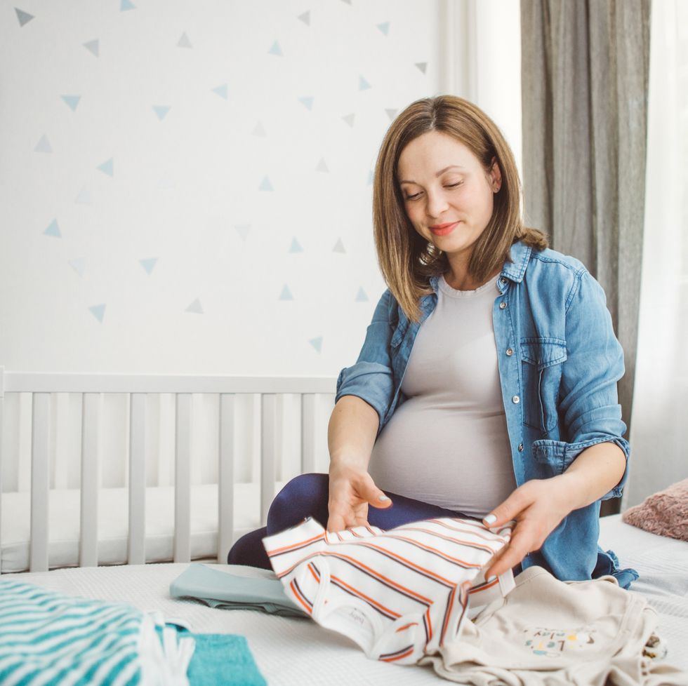 pregnant woman at home nesting by sorting baby clothes