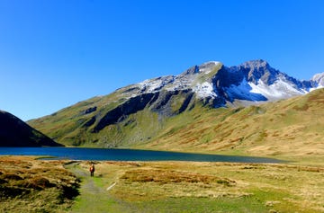 a person walking on a trail by a lake with a mountain in the background