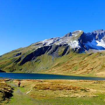 a person walking on a trail by a lake with a mountain in the background a person walking on a trail by a lake with a mountain in the background