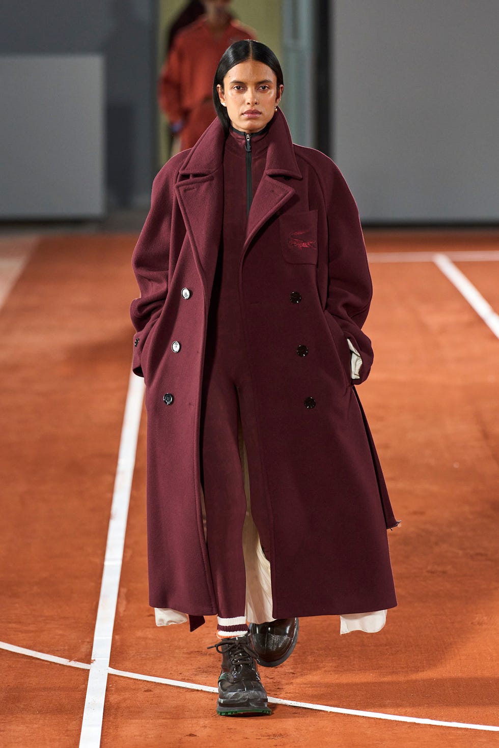 A model walks the catwalk wearing a burgundy coat and matching outfit