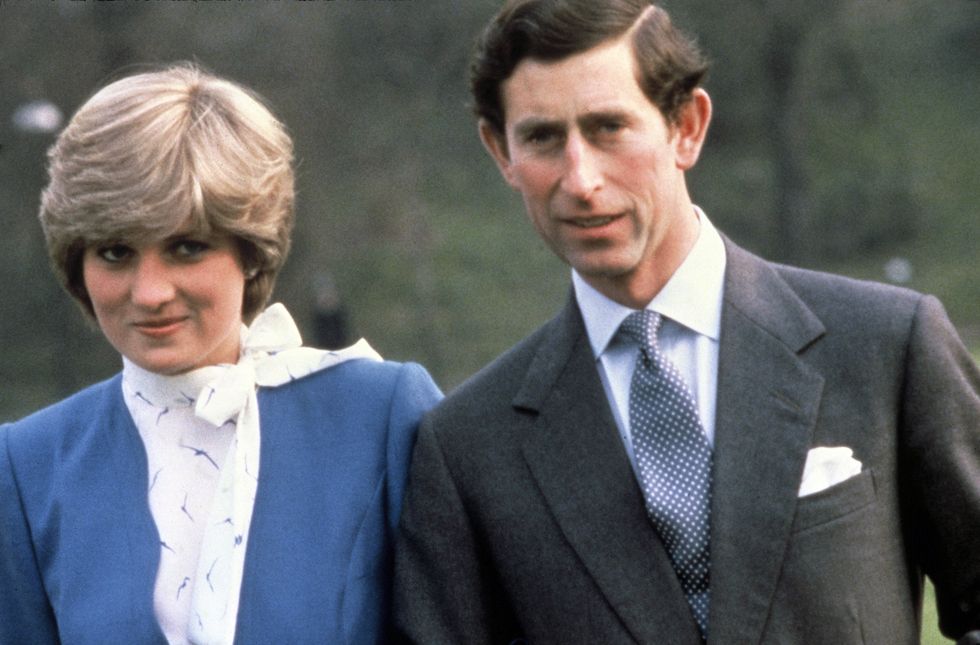 lady diana spencer, wearing a blue dress, and prince charles, wearing a gray suit, white shirt, and blue spotted tie, smiling while standing outside