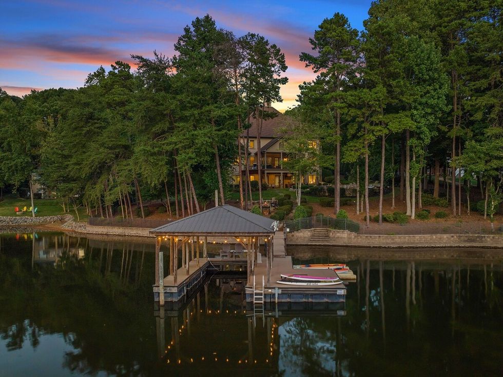 a house on a dock surrounded by water with trees and a building in the background