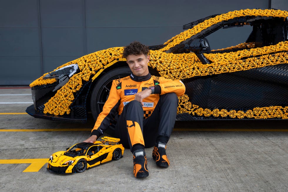 lando norris places his right hand on top of the lego technic mclaren p1 model as he sits on the floor in front of the lifesize version