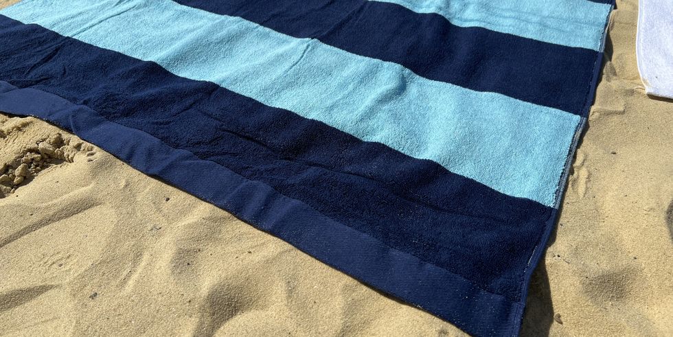 a navy and light blue striped lands' end cabana stripe beach towel laid out on the sand, good housekeeping's testing for the best beach towels