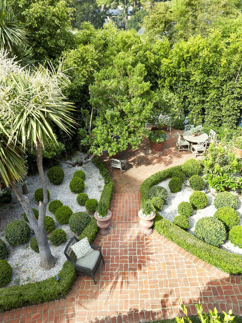 a creative landscaping idea showing plant beds edged in boxwood hedges and filled with pea gravel and rounded boxwood bushes for an effect that looks like green polka dots