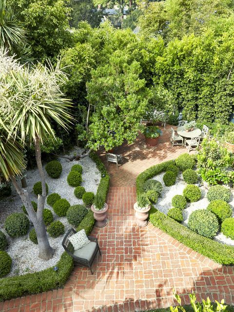 a creative landscaping idea showing plant beds edged in boxwood hedges and filled with pea gravel and rounded boxwood bushes for an effect that looks like green polka dots