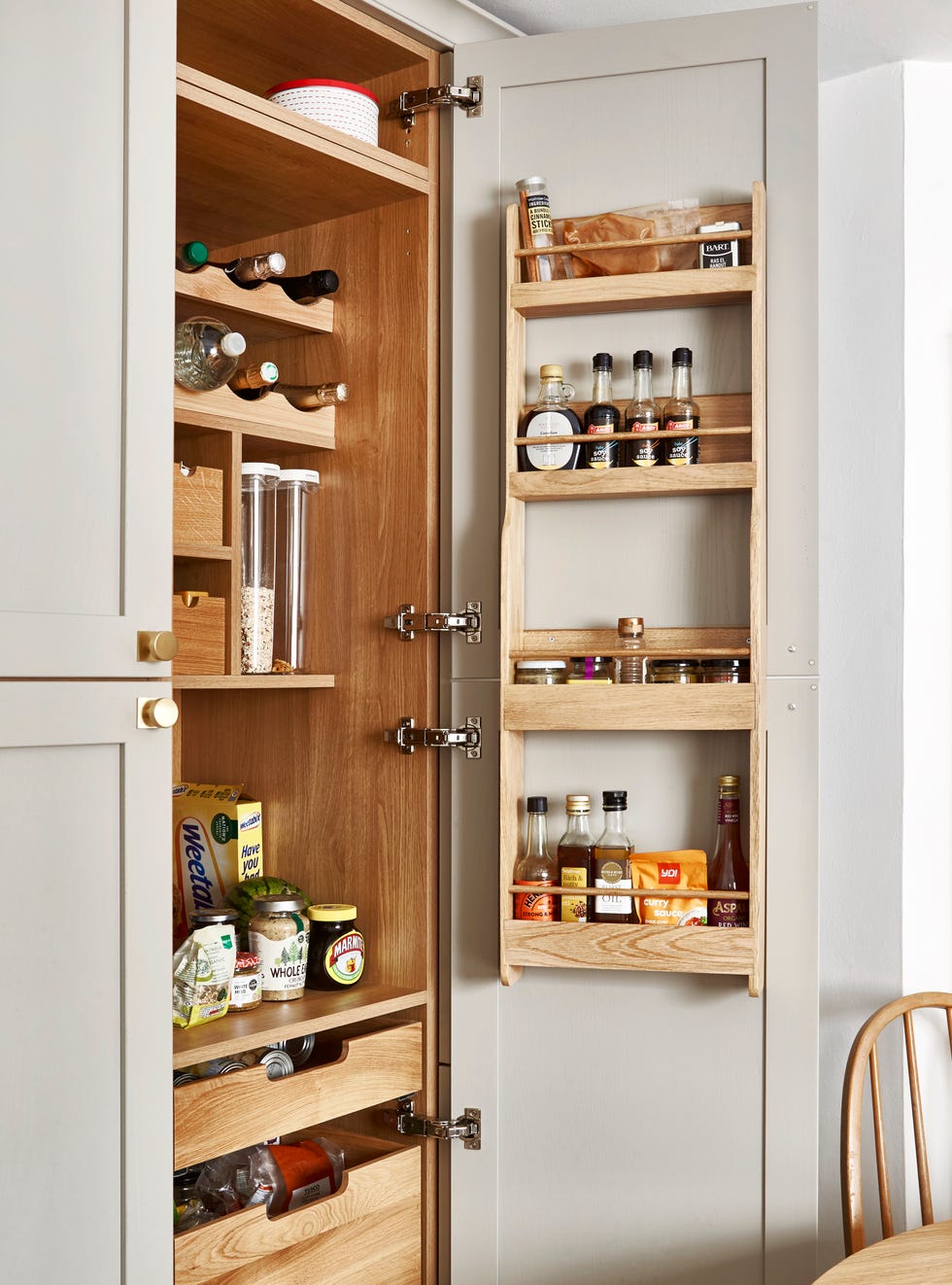 Food storage cabinet with shelves filled with dry goods, spices and oils in a soft grey Scandinavian style kitchen