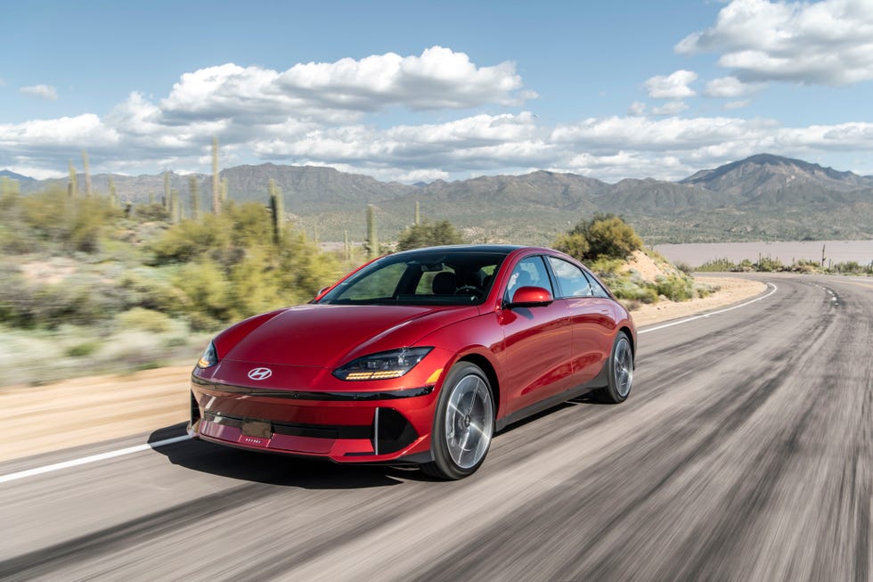 red car driving on a desert road with mountains in the background
