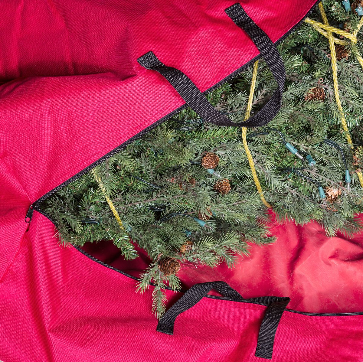 large artificial christmas tree being placed in red nylon zipper bag