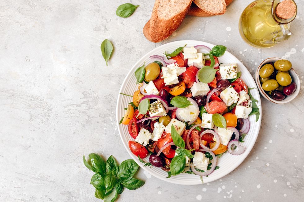 large portion of appetizing greek salad with feta cheese, fresh tomatoes, basil, onion olives and olive oil, healthy food.