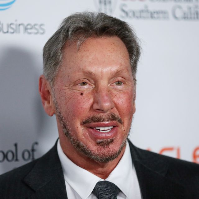 larry ellison smiles and looks past the camera, he is wearing a black suit jacket, white collared shirt and black and white tie