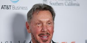 larry ellison smiles and looks past the camera, he is wearing a black suit jacket, white collared shirt and black and white tie