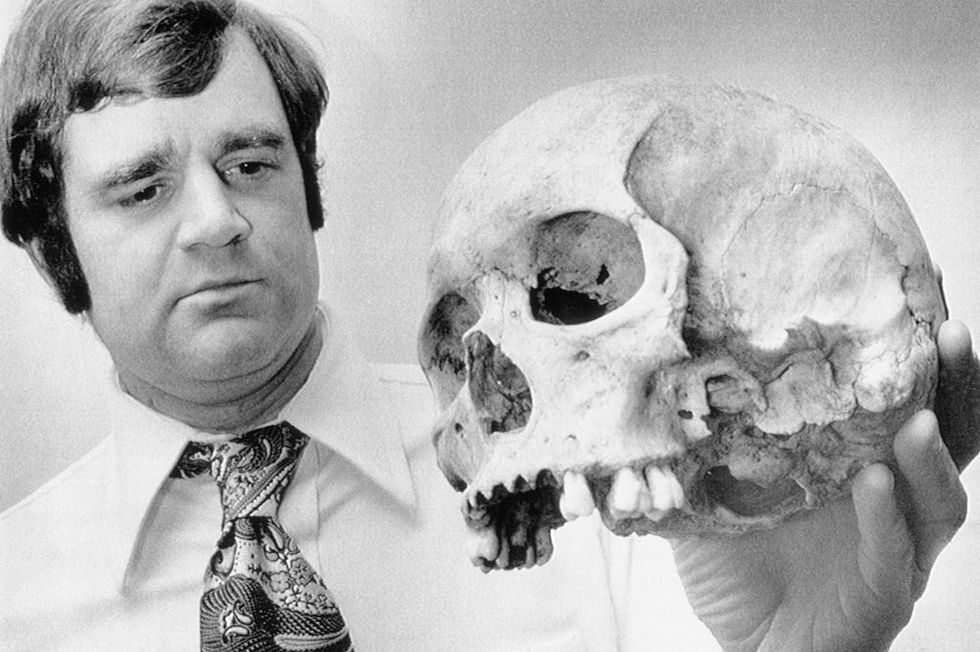 a man in a collared shirt and tie holds a skull