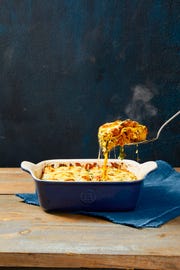 a slice of cheesy spinach meat lasagna being taken out of the baking dish