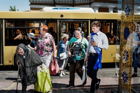 Passagiers van verschillende leeftijden stappen uit een stadsbus en gaan op weg naar de ceremonie van de Laatste Bel