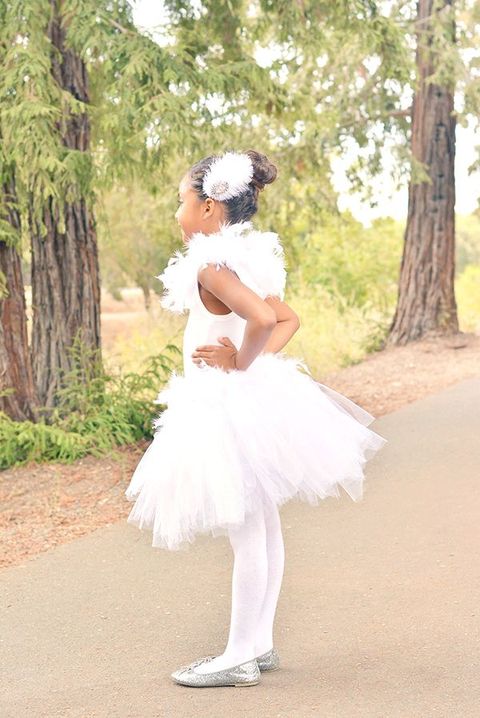 little girl in white swan costume with white tulle skirt, white tights, silver shoes, and feather headpiece and collar