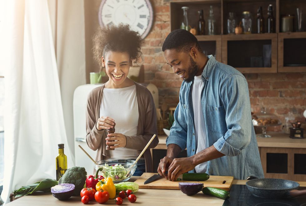 Laughing black couple preparing salad in kitchen