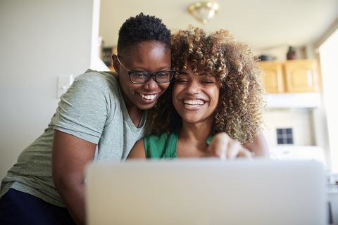 laughing black women hugging and using laptop