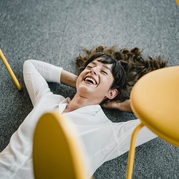 laughing businesswoman laying in an office on the floor between chairs