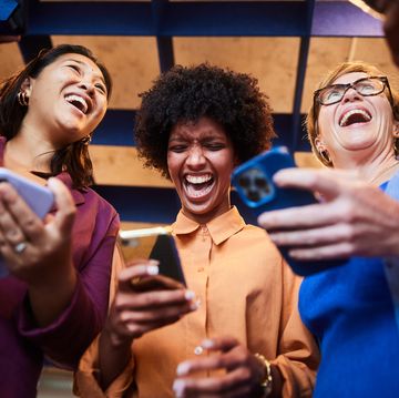 laughing businesswomen checking their phones while standing in an office
