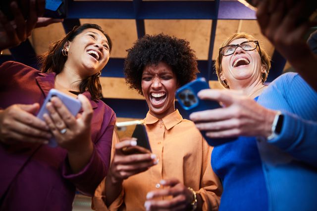 laughing businesswomen checking their phones while standing in an office