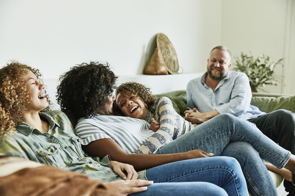 laughing daughter embracing mother while sitting on couch with family in living room