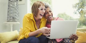 Laughing mature women sharing laptop on living room sofa