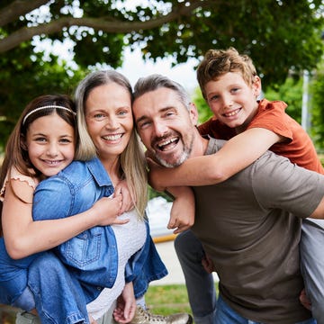 laughing parents carrying their children on their back outside in their yard