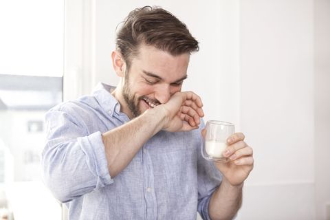 Laughing young man with glass of milk wiping his mouth