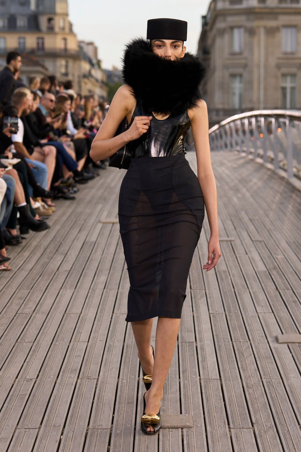a woman wearing a black dress and black hat walking on a wooden deck
