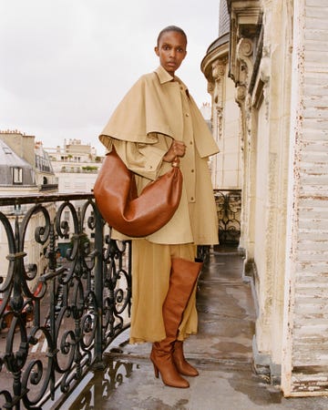 person posing on a balcony wearing a stylish outfit and holding a large bag